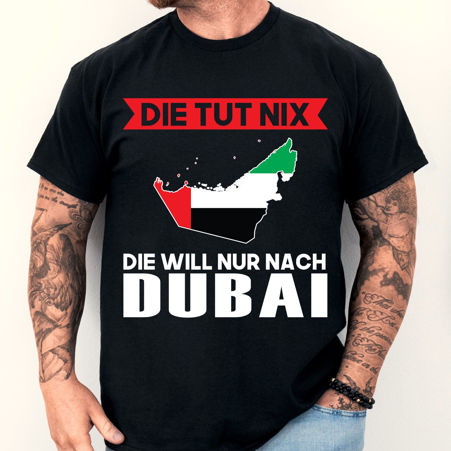 Mann trägt ein T-Shirt mit der Aufschrift 'Dubai Shirt | Die tut nix Geschenk' und einer stilisierten Dubaischen Flagge.