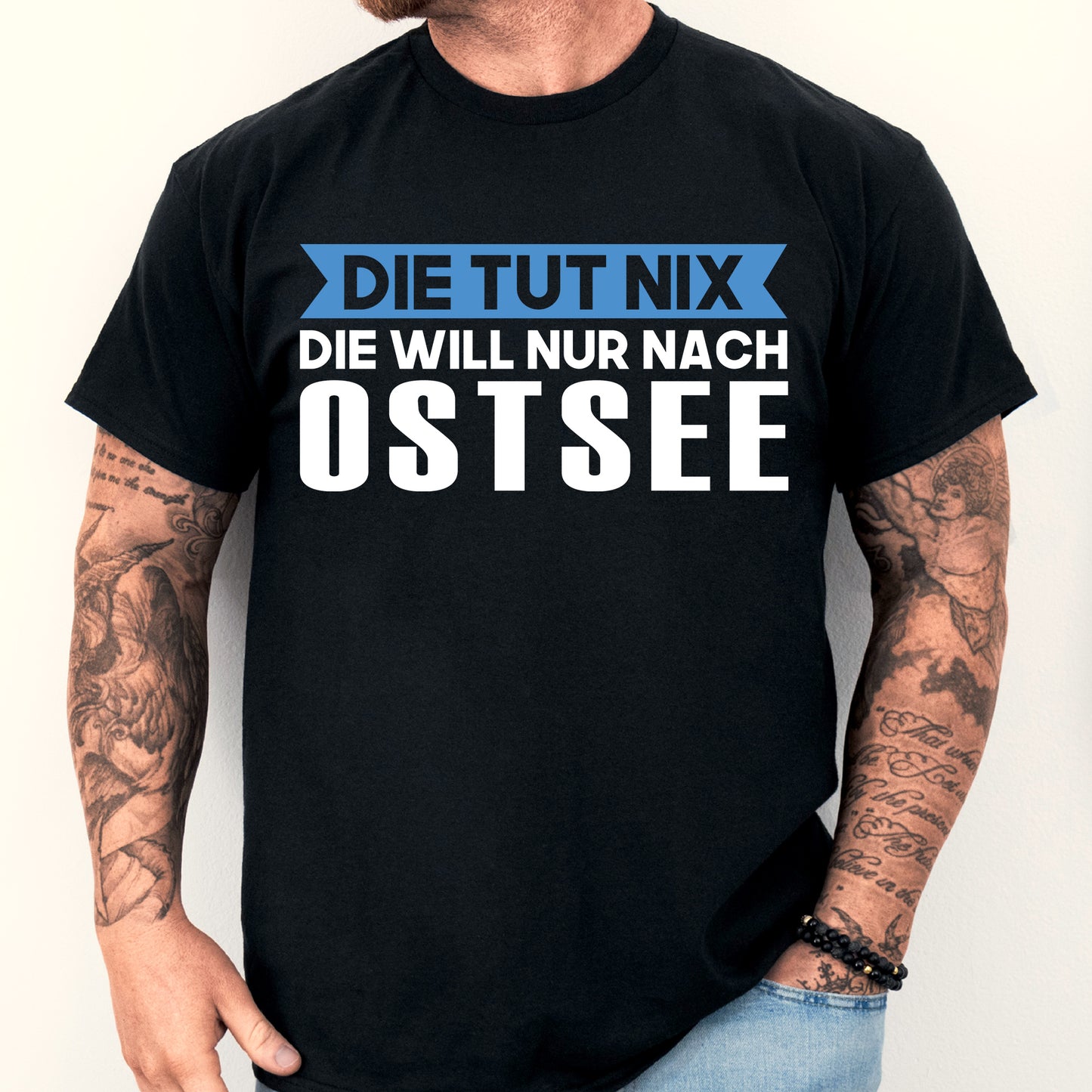 Mann trägt ein T-Shirt mit der Aufschrift "Ostsee Shirt | Die tut nix Ostsee Geschenk Ostdeutsch Deutschland".