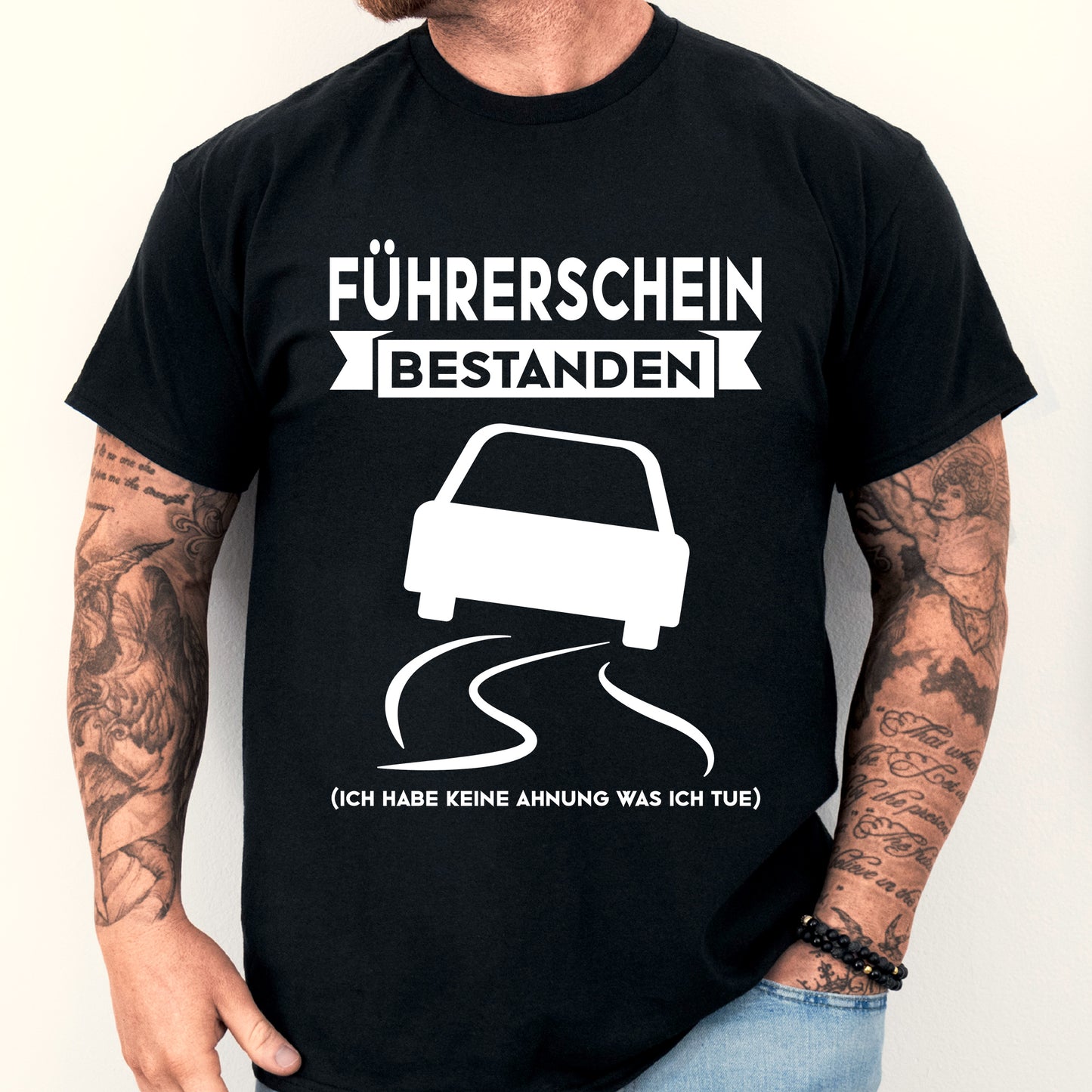 Mann trägt ein T-Shirt mit der Aufschrift "Führerschein bestanden" als Geschenk zur bestandenen Prüfung.