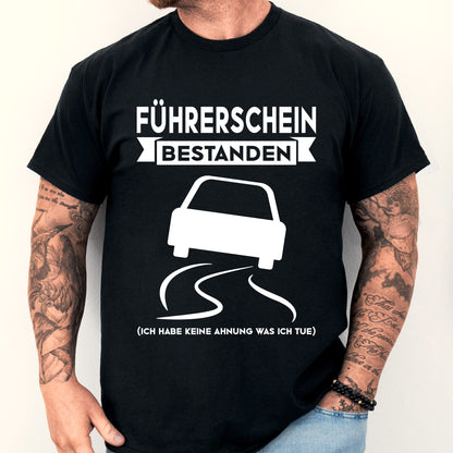 Mann trägt ein T-Shirt mit der Aufschrift "Führerschein bestanden" als Geschenk zur bestandenen Prüfung.
