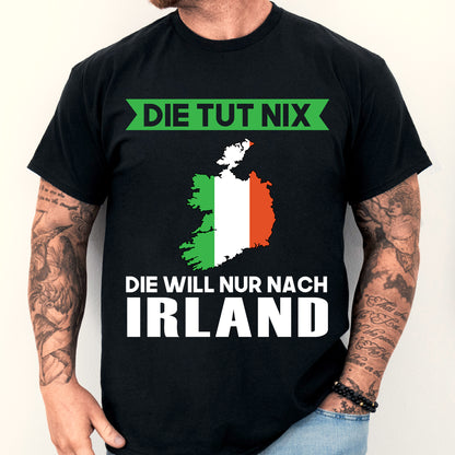 Mann trägt ein grünes T-Shirt mit der Aufschrift "Die tut nix, er will nur saufen" und einem irischen Kleeblatt-Design.