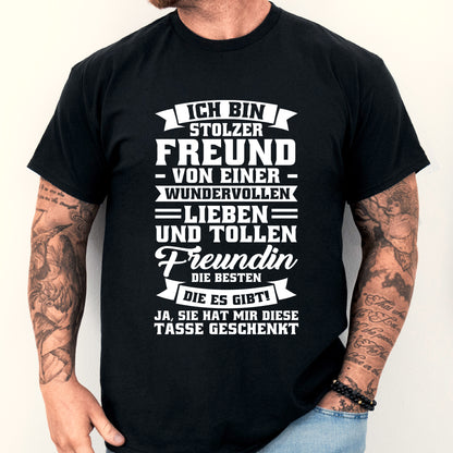 Mann trägt ein T-Shirt mit der Aufschrift "Ich bin stolz auf meine tolle Freundin" und hält eine Tasse, die Freundschaft symbolisiert.